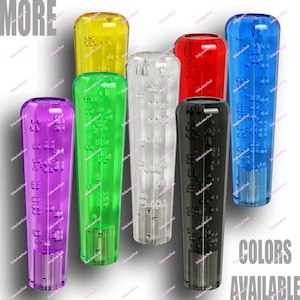 Puede incluir: Una colección de pomos de cambio transparentes y coloridos. Los pomos están disponibles en morado, verde, amarillo, transparente, rojo, negro y azul. Las palabras "MORE" y "COLORS AVAILABLE" están presentes.