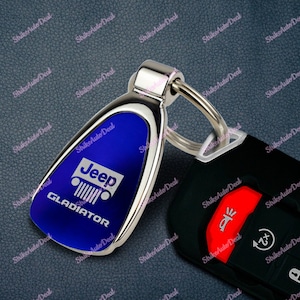 May include: A blue Jeep Gladiator key chain with a silver metal ring. The keychain has a blue background with the Jeep logo and the word "GLADIATOR" in white lettering.
