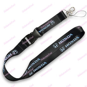 May include: Black lanyard with the Honda logo and text in light blue. The lanyard has a black plastic buckle and a silver-colored metal clip. The text "HONDA" is repeated along the length of the lanyard.