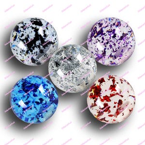 以下が含まれることがあります： カラフルな紙吹雪のようなインクルージョンが入った、透明な球形のガラスオブジェクトが5つ。色は黒、銀、紫、青、赤など。白い背景に円形に配置されています。