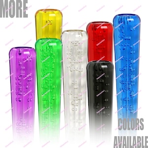 May include: A selection of transparent shift knobs in various colours. The knobs feature a bubble design and are available in yellow, green, clear, red, black, purple, and blue. The image includes the text "MORE" and "COLORS AVAILABLE".