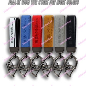May include: Six leather keychains with metal rings. Each keychain has a different color: black, blue, red, brown, gray, and white. The keychains have Japanese text that reads "藤原とうふ店 (自家用)".