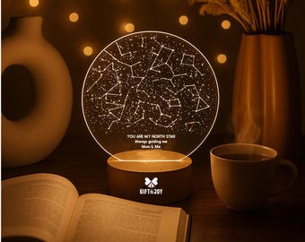 Może przedstawiać: Okrągła lampka nocna z akrylu z białym wzorem mapy gwiazd i konstelacji. Tekst brzmi: YOU ARE MY NORTH STAR, Always guiding me, Mum & Me. Podstawa jest cylindryczna i jasna, z białym logo GIFT N JOY umieszczonym na jej froncie.