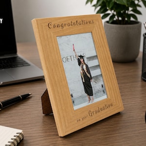 May include: A light-colored wooden picture frame with a beveled edge, featuring the engraved text "Congratulations" at the top and "on your Graduation" at the bottom. The frame holds a photograph of a graduate in a cap and gown holding a diploma.