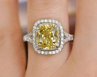 May include: A yellow cushion-cut diamond engagement ring with a double halo of smaller diamonds. The ring is set in white gold.