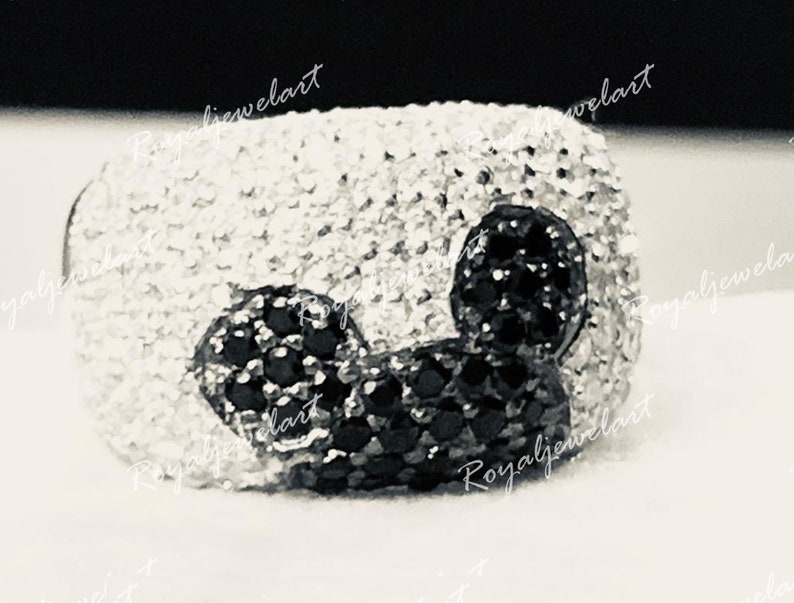 K&ouml;nnte beinhalten: Ein silberner Ring mit einem schwarzen und wei&szlig;en Mickey Mouse Design. Der Ring ist mit kleinen, funkelnden Steinen besetzt.