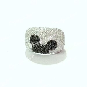 K&ouml;nnte beinhalten: Ein silberner Ring mit einem Mickey-Maus-Design aus schwarzen Diamanten. Der Ring ist mit wei&szlig;en Diamanten besetzt.