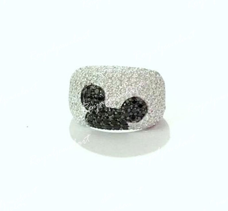 K&ouml;nnte beinhalten: Ein silberner Ring mit einem Mickey-Maus-Design aus schwarzen Diamanten. Der Ring ist mit wei&szlig;en Diamanten besetzt.