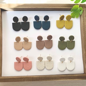 May include: A set of 10 pairs of handmade polymer clay earrings. The earrings are in various colors, including black, blue, brown, beige, pink, green, white, and yellow. Each pair features a small circle on top of a larger half-circle shape.