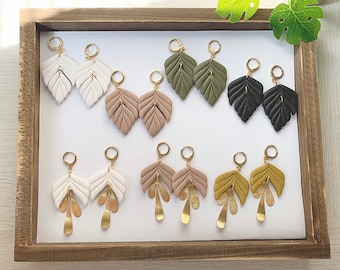 May include: A set of 10 pairs of leaf-shaped earrings with gold accents. The earrings are made of polymer clay and come in various colors, including white, beige, green, and black.