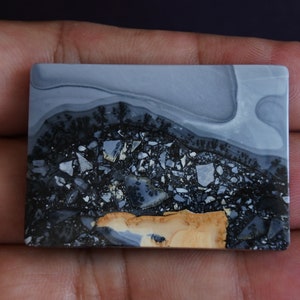 May include: A polished, rectangular slab of gray, black, and tan agate with a dendritic pattern. The agate has a layered appearance with a smooth, polished surface.