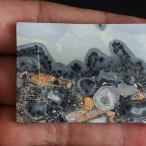 May include: A close-up of a polished, gray, black, and orange agate slab with a unique, swirling pattern. The slab has a smooth, polished surface and is approximately 2 inches by 3 inches.
