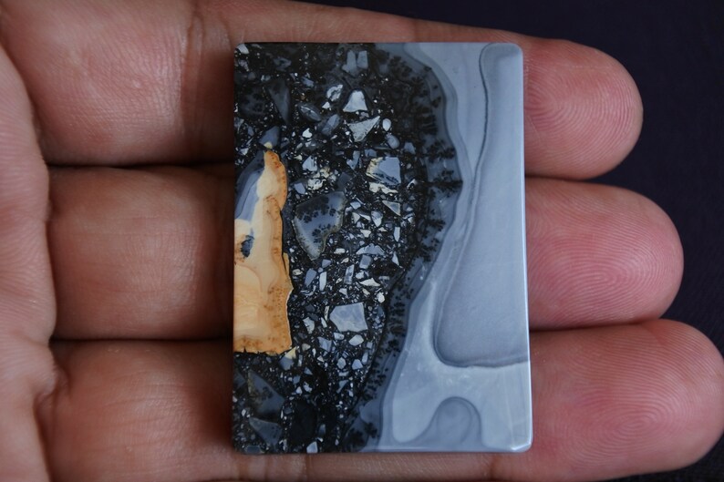May include: A rectangular, polished stone with a gray, white, and black pattern. The stone has a brown, orange, and black section on the left side.
