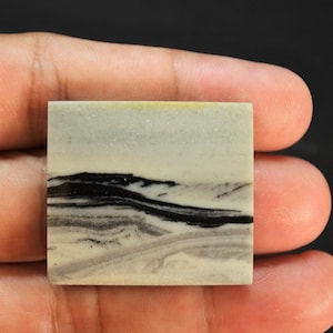 May include: A square-shaped stone cabochon featuring a smooth, matte surface with a natural landscape pattern. The stone displays horizontal bands of cream, light grey, and dark black colours, creating a distinct layered appearance across the face.