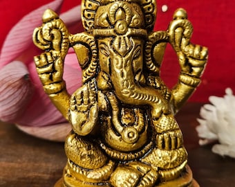 Puede incluir: Una estatua de metal dorada de Ganesha, el dios hindú de la sabiduría y la prosperidad. La estatua está sentada sobre una base con un diseño decorativo. La estatua está intrincadamente detallada y tiene un estilo indio tradicional.