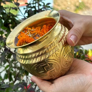 Puede incluir: Un cuenco de metal dorado con diseños intrincados y pétalos de flores naranjas flotando en el agua.