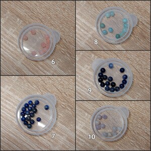 Puede incluir: Cinco peque&ntilde;os recipientes de pl&aacute;stico transparente con tapas, cada uno con cuentas de piedras preciosas de diferentes colores. Las cuentas son rosas, celeste, azul oscuro y lavanda. Los recipientes est&aacute;n etiquetados con los n&uacute;meros 6, 7, 8, 9 y 10.