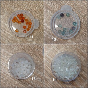 Puede incluir: Cuatro peque&ntilde;os recipientes de pl&aacute;stico transparente con tapas, cada uno con una colecci&oacute;n de cuentas. Las cuentas son de varios colores, incluyendo naranja, verde, morado y blanco. Los recipientes est&aacute;n etiquetados con los n&uacute;meros 11, 12, 13 y 14.