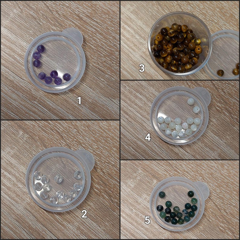 Puede incluir: Cinco peque&ntilde;os recipientes de pl&aacute;stico transparente contienen cada uno un tipo diferente de cuentas de piedras preciosas. Las cuentas son moradas, marrones, transparentes, blancas y verde oscuro. Los recipientes est&aacute;n dispuestos sobre una superficie de madera marr&oacute;n claro.