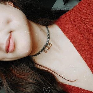 Puede incluir: Primer plano de un collar gris oscuro y dorado con peque&ntilde;os abalorios. El collar se lleva sobre un su&eacute;ter rojo. La imagen tiene un efecto suave y filtrado con un coraz&oacute;n dibujado en el pelo.