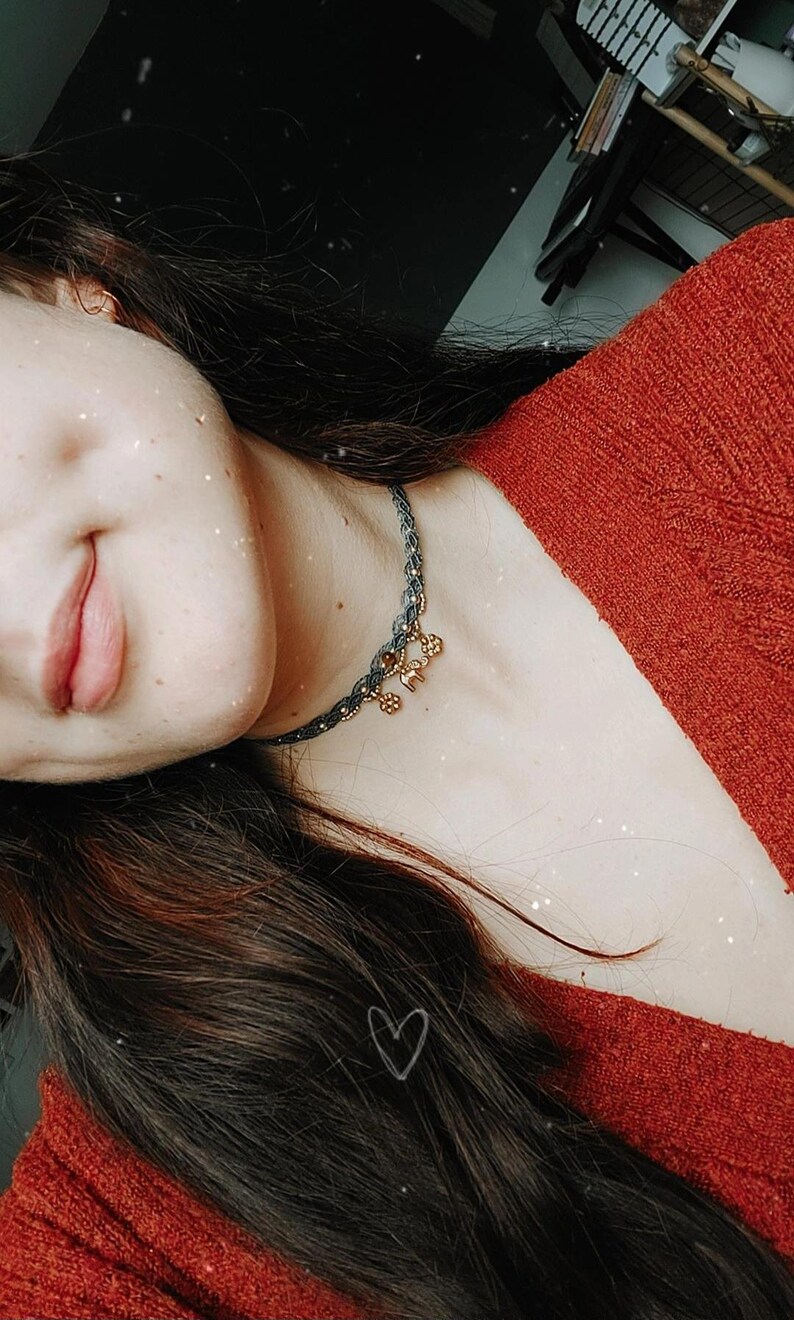 Puede incluir: Primer plano de un collar gris oscuro y dorado con peque&ntilde;os abalorios. El collar se lleva sobre un su&eacute;ter rojo. La imagen tiene un efecto suave y filtrado con un coraz&oacute;n dibujado en el pelo.