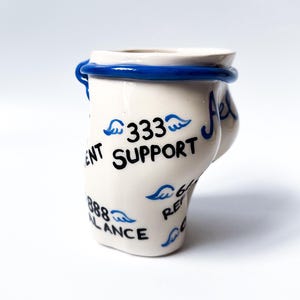 May include: White ceramic mug with blue trim and black writing. The writing includes "333 Support", "888 Balance", and "666 Refer".