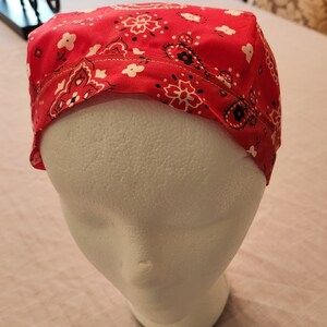 May include: Red bandana with a white and black paisley pattern. The bandana is folded and placed on a white mannequin head.