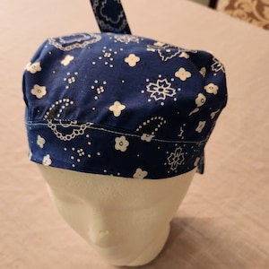May include: A blue bandana with a white paisley pattern. The bandana is folded and tied to create a cap.