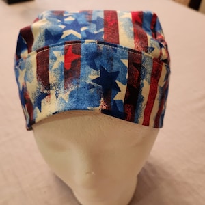 May include: A red, white, and blue patterned scrub hat with stars and stripes. The hat is made of a soft, comfortable fabric and is perfect for nurses, doctors, and other healthcare professionals.