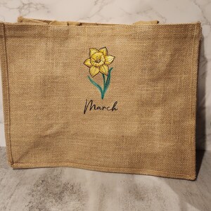 May include: A brown burlap tote bag with a yellow daffodil and the word "March" embroidered on the front.