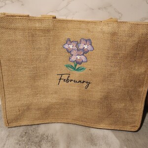 May include: A brown burlap tote bag with a floral design and the word "February" embroidered on it.