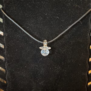 May include: A clear glass pendant with a faceted design hangs from a black cord necklace.