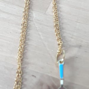 May include: A gold chain necklace with a gold spatula charm. The spatula has a blue handle and white blade.