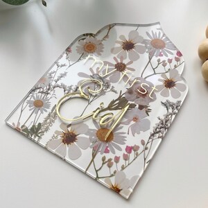May include: A clear acrylic sign with a floral pattern and gold lettering that says "my first Eid".