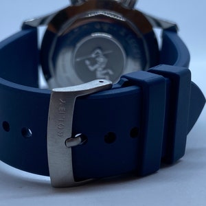 May include: A blue rubber watch strap with a silver buckle. The buckle has the text "COL-18" engraved on it.