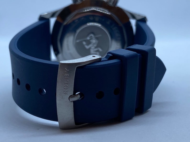 May include: A blue rubber watch strap with a silver buckle. The buckle has the text "COL-18" engraved on it.