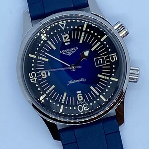 May include: A silver Longines watch with a blue face and a blue rubber strap. The watch has a date window at 3 o'clock and the words "Longines" and "Automatic" printed on the face.