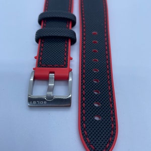 Puede incluir: Correa de reloj negra con costuras rojas y una hebilla plateada. La hebilla tiene la palabra "GOLIA" grabada.