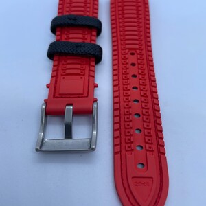 Puede incluir: Correa de reloj roja y negra con hebilla plateada. La correa tiene un dise&ntilde;o texturizado y el texto "20-18" est&aacute; impreso en la parte inferior.