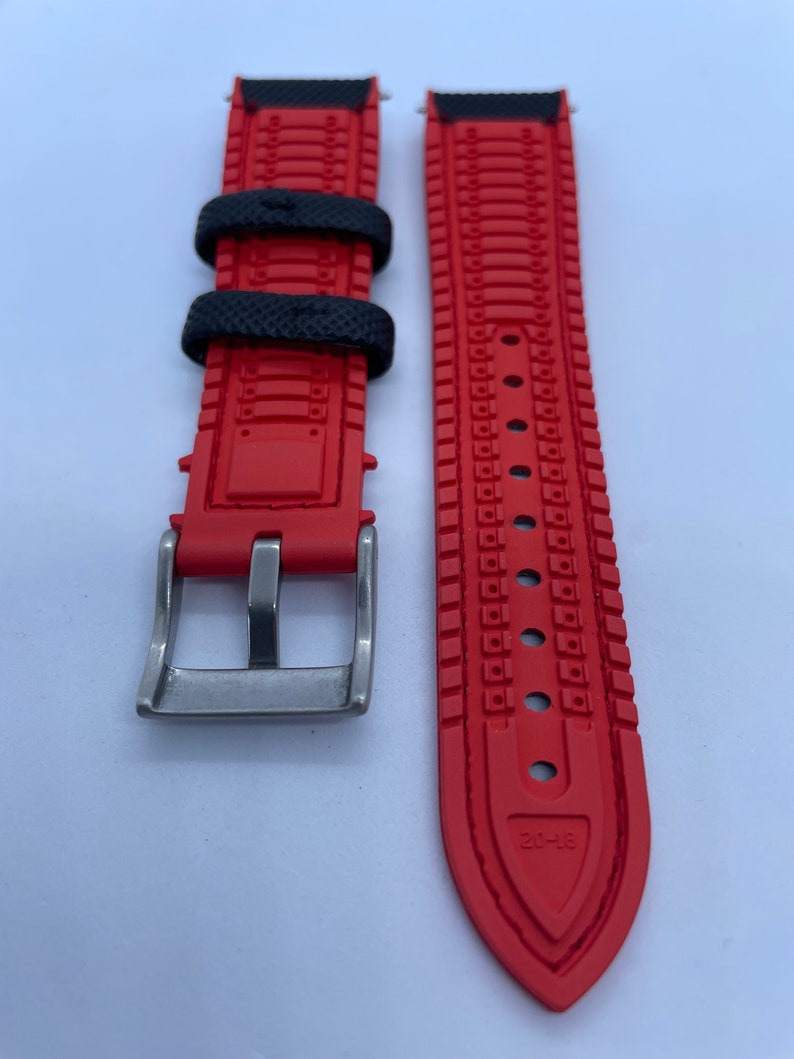 Puede incluir: Correa de reloj roja y negra con hebilla plateada. La correa tiene un dise&ntilde;o texturizado y el texto "20-18" est&aacute; impreso en la parte inferior.