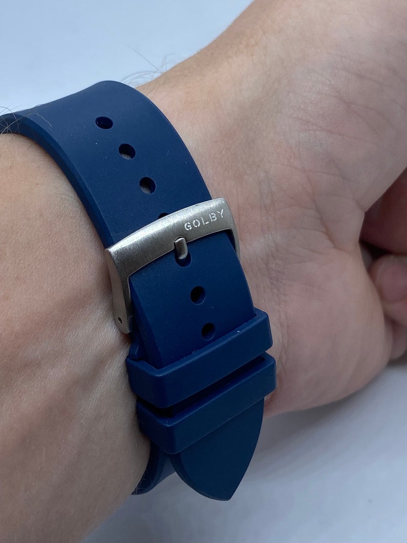 May include: A blue silicone watch strap with a silver buckle that says "GOLBY" on it.