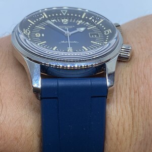 May include: A silver Longines watch with a blue face and a blue rubber strap. The watch has a date window at the 3 o'clock position and a chronograph function.