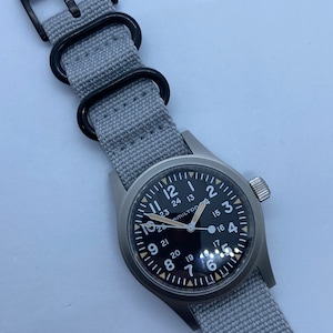 20 mm e 22 mm, pulseira estilo cinto de segurança cinza com fecho e ferragens pretos.