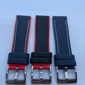 Puede incluir: Tres correas de reloj con una tela azul texturizada y costuras rojas o blancas. Las correas tienen hebillas plateadas con la palabra "GOLDBY" grabada en ellas.