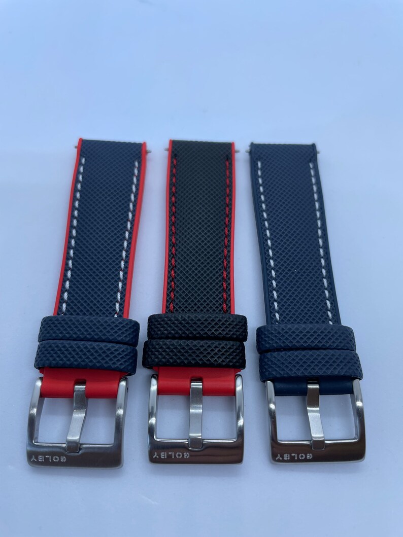 Puede incluir: Tres correas de reloj con una tela azul texturizada y costuras rojas o blancas. Las correas tienen hebillas plateadas con la palabra "GOLDBY" grabada en ellas.