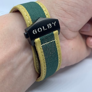 Peut inclure: Un bracelet de montre rayé vert et jaune avec une boucle noire sur laquelle est inscrit "GOLIBY" en lettres blanches.