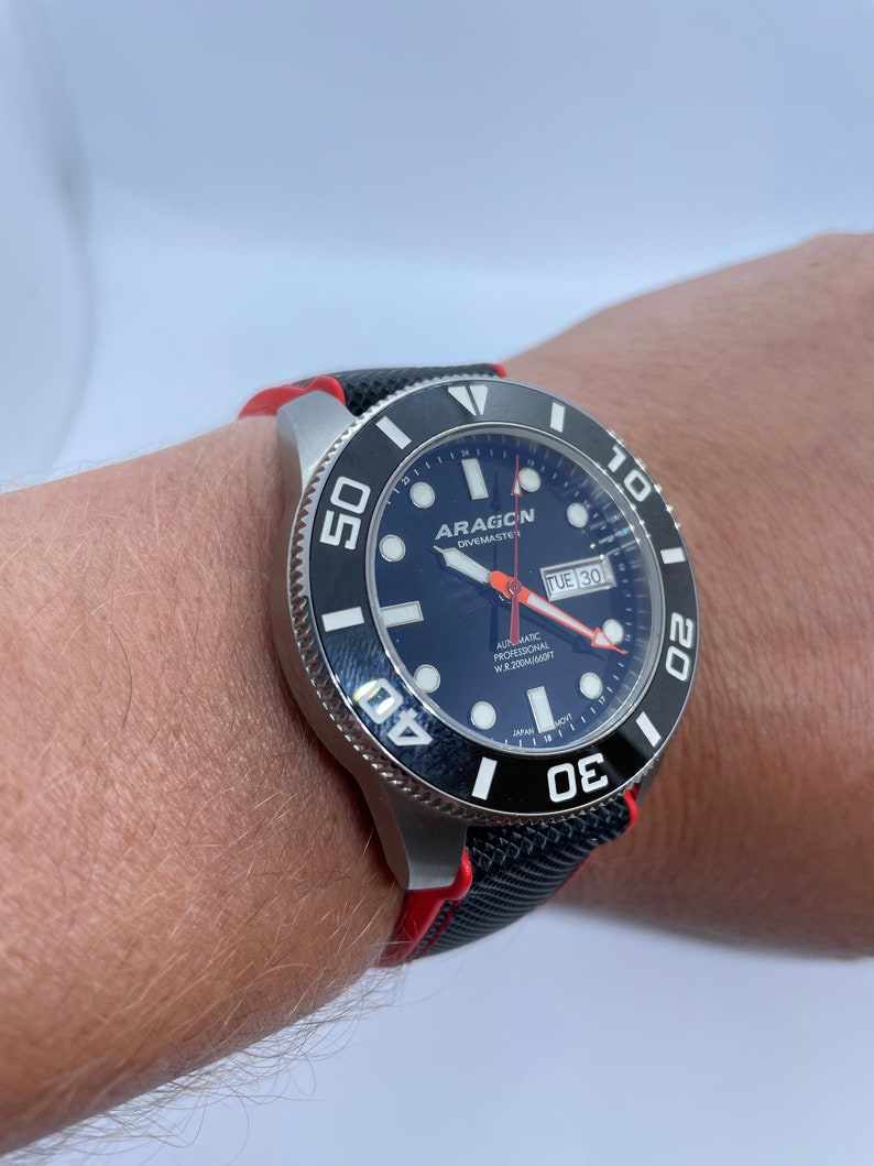 Puede incluir: Un reloj de pulsera negro y rojo con una esfera negra y marcas blancas. El reloj tiene un bisel giratorio con n&uacute;meros blancos y una ventana de fecha que dice "TUE 30". La esfera del reloj tambi&eacute;n tiene el texto "ARAGON DIVEMASTER" y "AUTOMATIC PROFESSIONAL WR 200M/660FT".