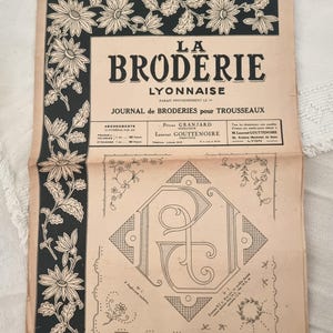 Può includere: Una rivista vintage aperta, intitolata "La Broderie Lyonnaise", con bordi floreali ed elementi decorativi. La copertina presenta testo in francese, incluso il nome della pubblicazione e la data "1 Octobre 1945."