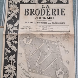 Può includere: Una rivista cartacea vintage intitolata La Broderie Lyonnaise datata 1 marzo 1930. La copertina presenta bordi floreali in bianco e nero, tipografia e vari motivi di monogrammi da ricamo tra cui le lettere RD, AG e BS su sfondo beige.