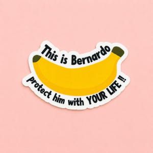 May include: A sticker featuring a yellow banana with green tips. The text "This is Bernardo, Protect him with YOUR LIFE !!" is written in black, following the banana's curve. The sticker is on a pink background.